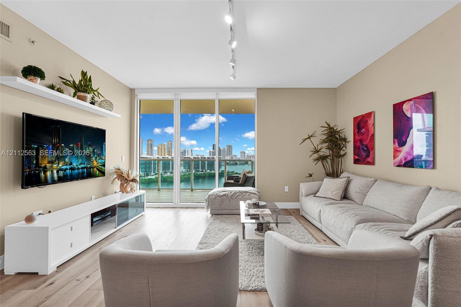 Living area featuring wood-finish flooring, floor-to-ceiling windows, a glass-panel balcony door, and a wall-mounted floating shelf