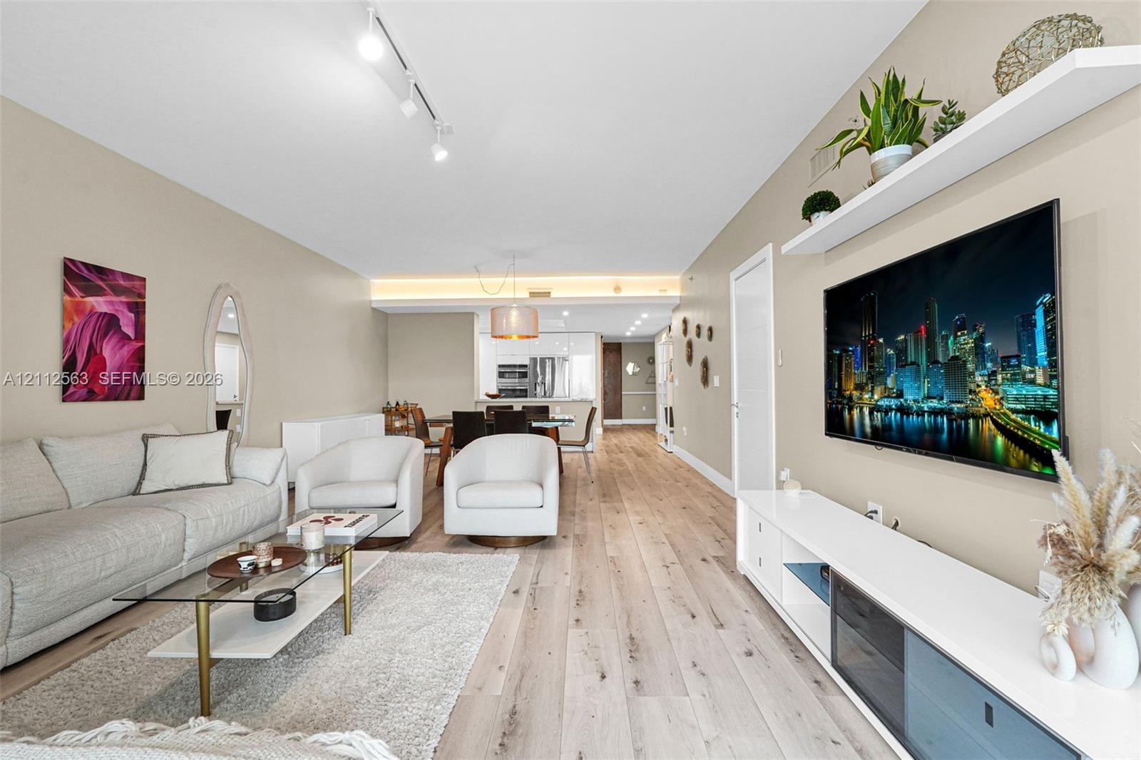 Open-concept room featuring wood-finish flooring, recessed track lighting, built-in wall-mounted shelving, and cove lighting