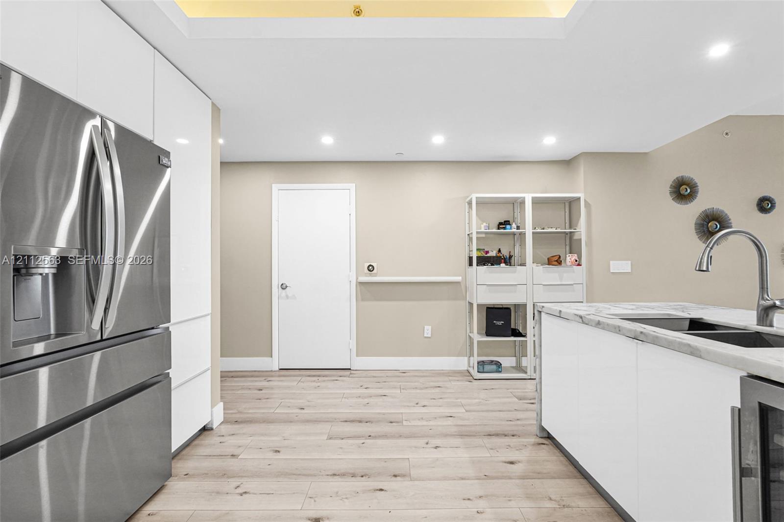 Kitchen featuring white flat-panel cabinetry, stainless steel refrigerator, stone-topped island with an integrated sink, wood-finish flooring, and recessed ceiling lighting