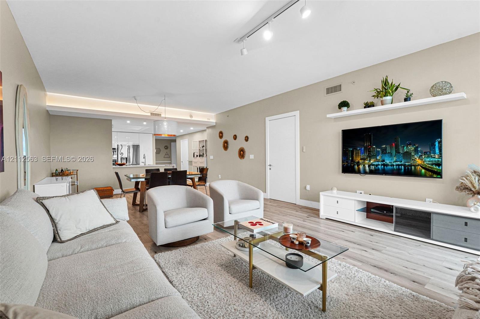 Open-concept living space featuring wood-finish flooring, cove lighting, adjustable track lighting, and a floating wall-mounted display shelf