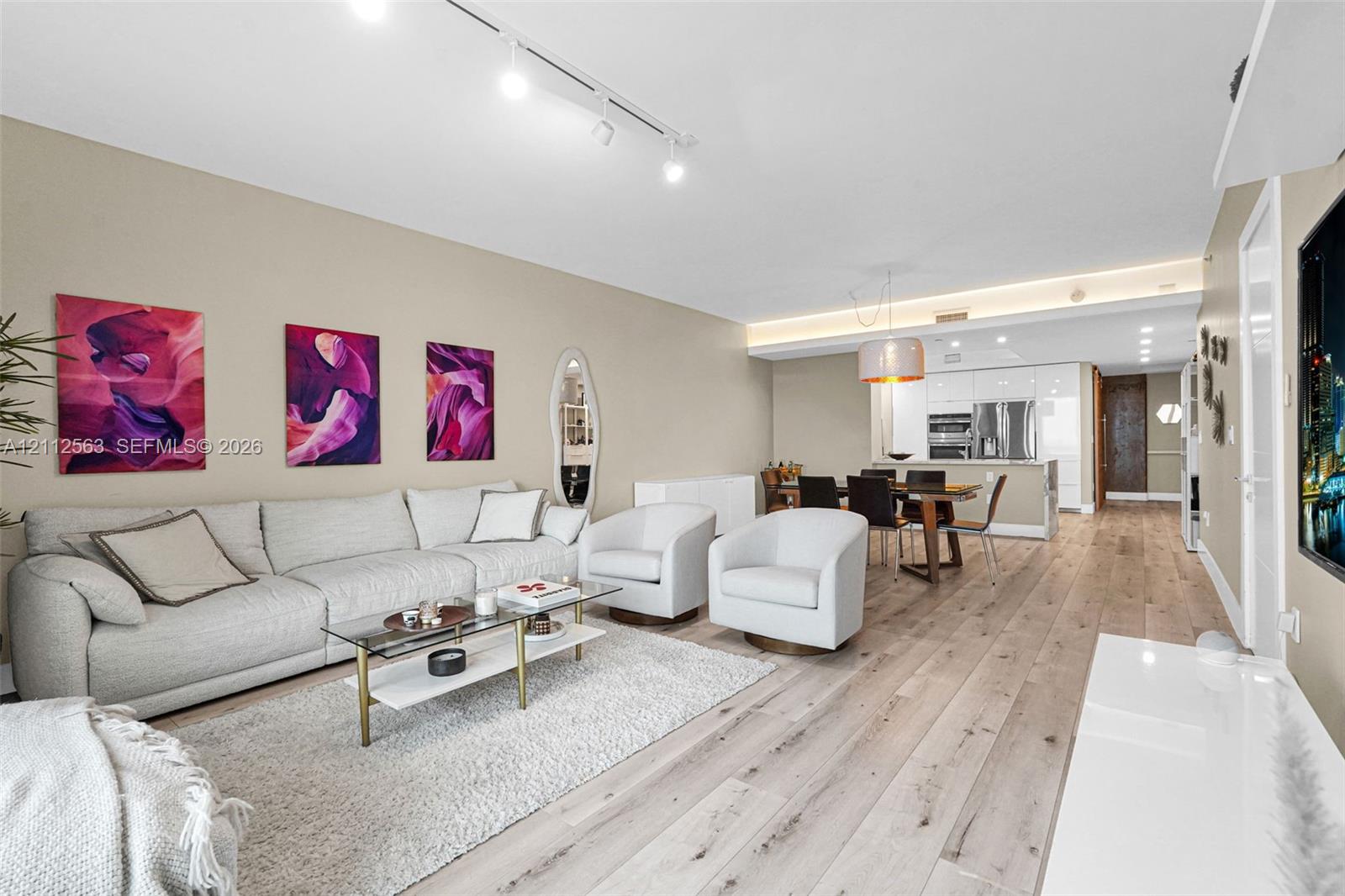Living area featuring wood-finish flooring, recessed lighting, track lighting, and cove ceiling detail with integrated illumination