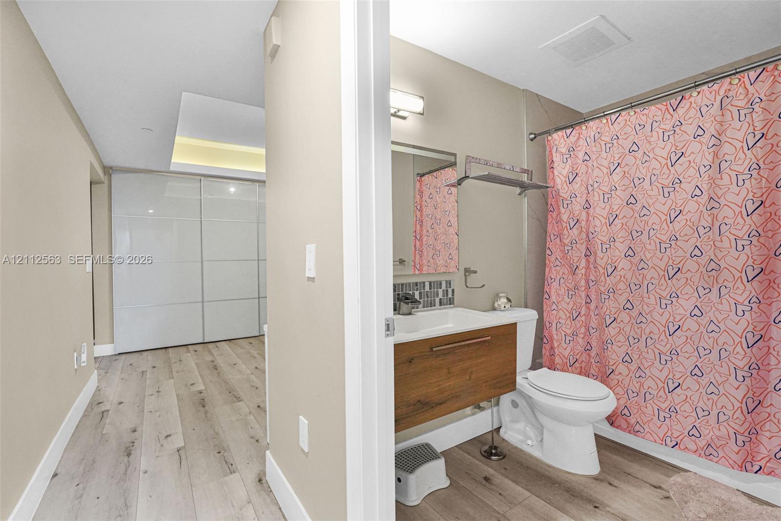 Bathroom featuring a wood-finish floating vanity, integrated sink, tiled backsplash, and recessed lighting, with wood-finish flooring extending into the area