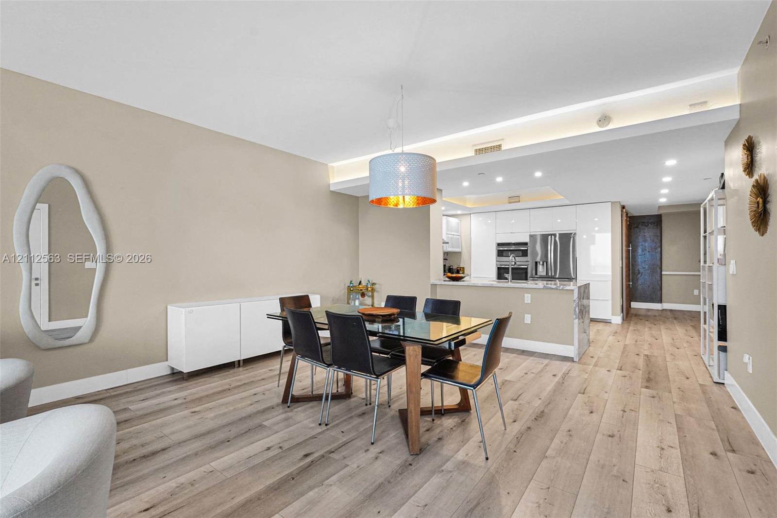 Open-concept interior featuring light wood-finish flooring, recessed ceiling lighting, a contemporary pendant light fixture, and high-gloss white cabinetry