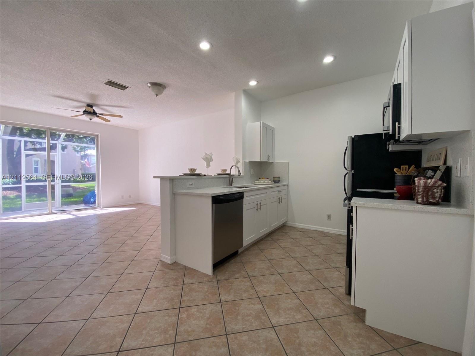 Kitchen featuring white shaker-style cabinetry, stainless steel dishwasher, tile flooring, and recessed lighting, with sliding glass doors opening to a screened enclosure