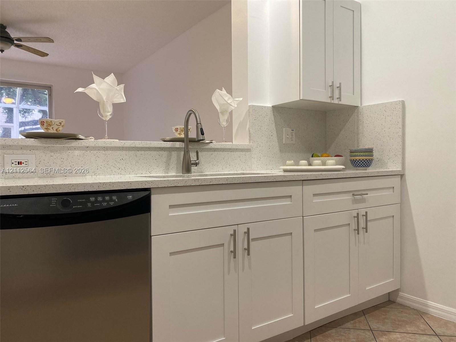 Kitchen featuring white shaker-style cabinetry, speckled solid-surface countertops, a stainless steel dishwasher, and a gooseneck pull-down faucet