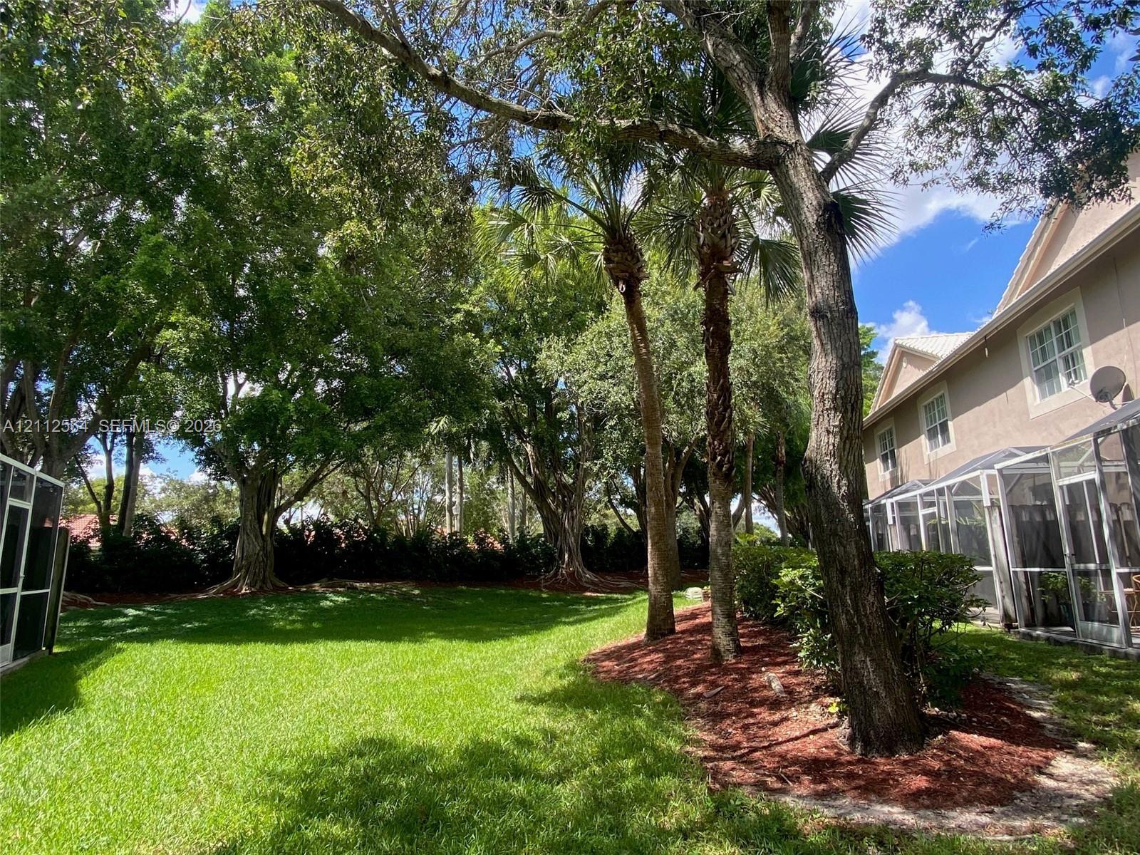 Expansive backyard featuring a sprawling lawn, mature trees, tiered landscaping, and a screened-in rear patio enclosure