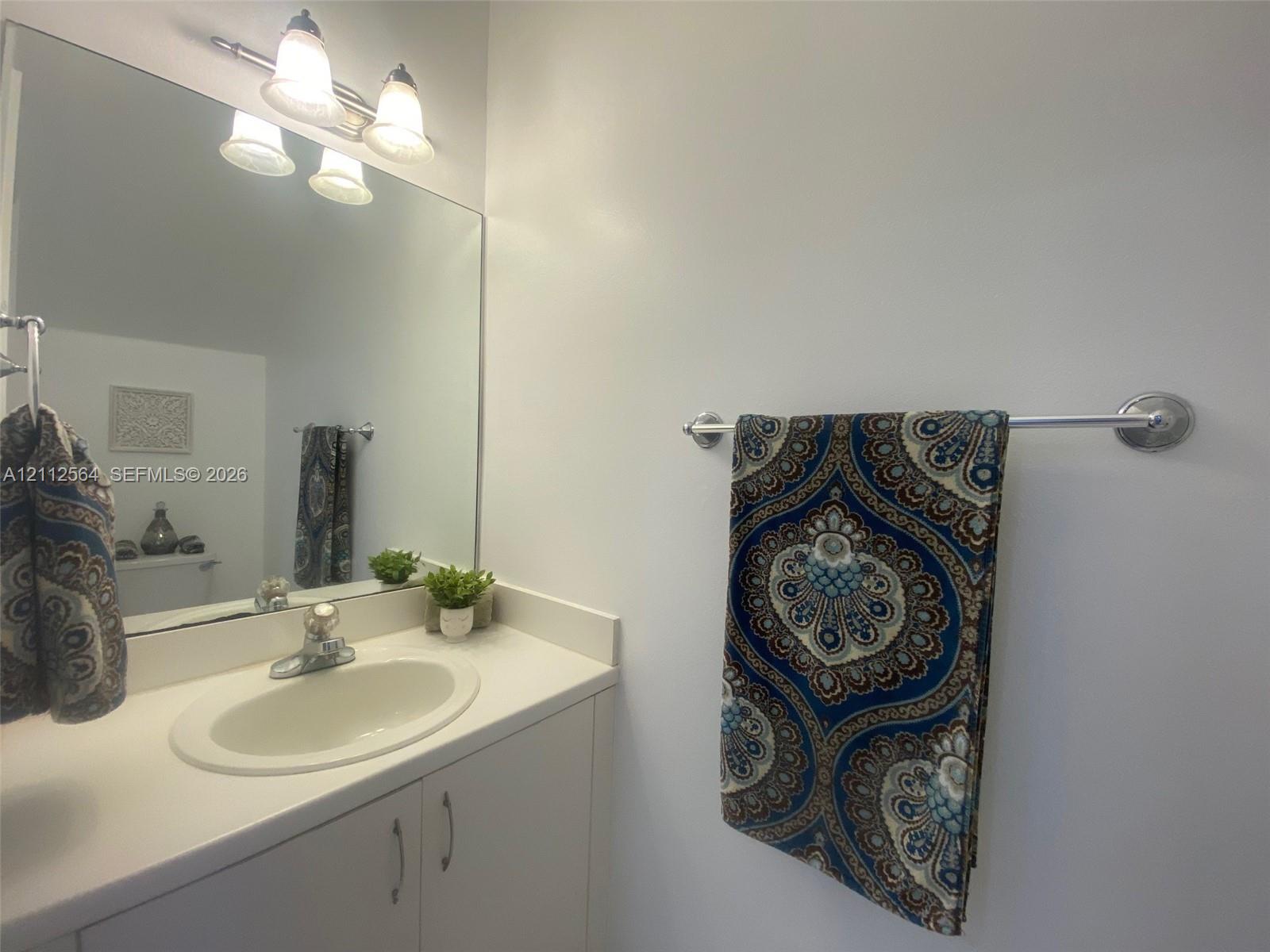 Vanity featuring an integrated sink, solid-surface countertop, cabinetry with silver-finish hardware, a large wall-mounted mirror, and a three-light fixture