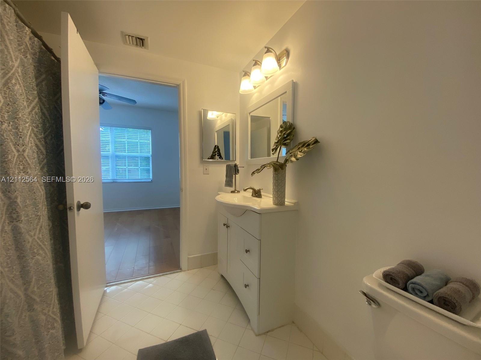 Bathroom featuring a white vanity cabinet with a curved basin, wall-mounted vanity lighting, a framed mirror, and tiled flooring