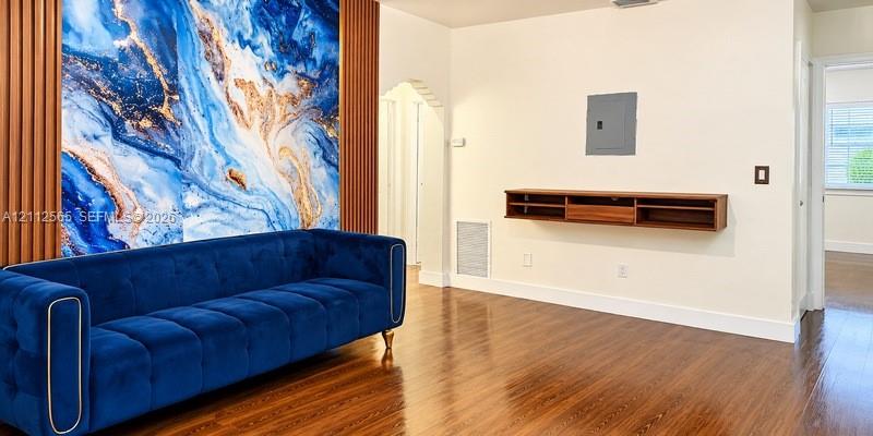 Polished wood-finish flooring, decorative wall mural with vertical wood-slat trim, arched entryway, and wall-mounted wood-finish media console