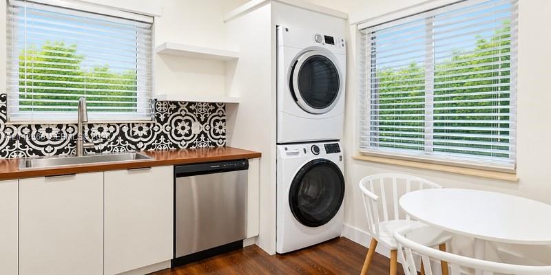 Laundry space featuring a stacked washer and dryer, wood-finish countertop, patterned tile backsplash, stainless steel dishwasher, and built-in shelving