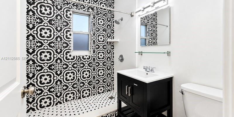 Bathroom featuring a black-and-white patterned tile shower surround, black vanity cabinet with an integrated white sink, rectangular wall mirror, and overhead vanity lighting