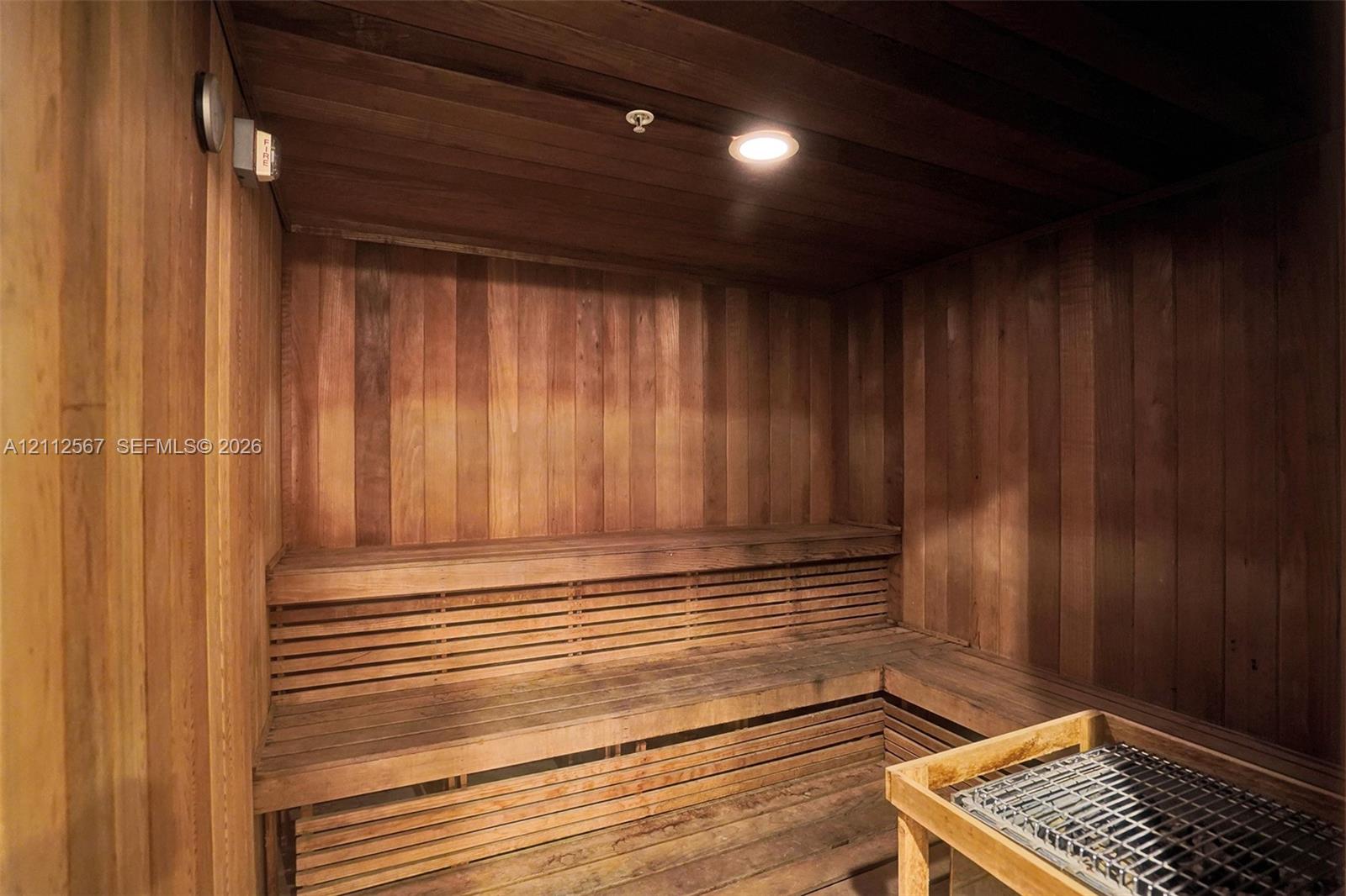 Sauna featuring natural wood paneling, multi-level slatted benches, and a dedicated heating unit
