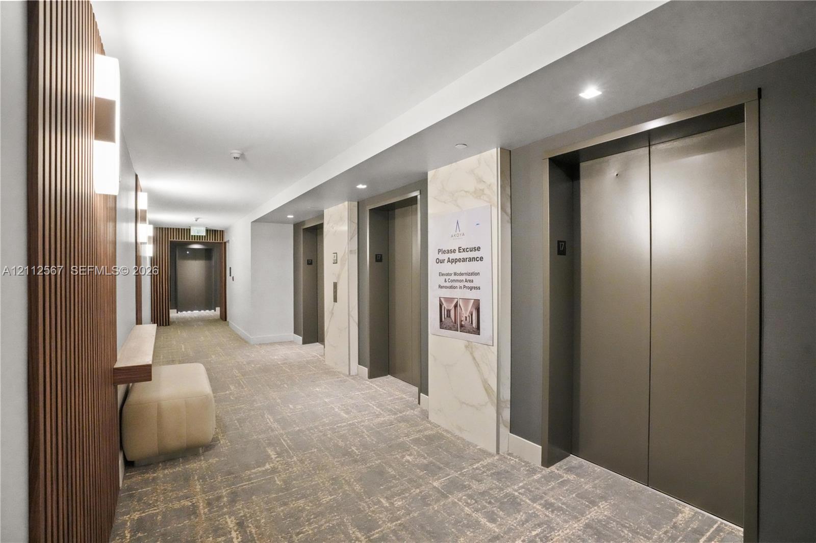 Common area featuring multi-panel elevator banks, vertical wood slat wall detailing, stone-clad pillar accents, recessed ceiling lighting, and wall-mounted light fixtures