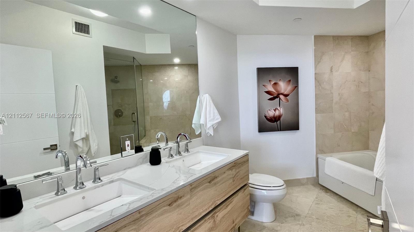 Double floating vanity with integrated rectangular sinks, polished stone-finish countertop, wood-finish cabinetry, recessed lighting, and a walk-in glass-enclosed shower with tile surround