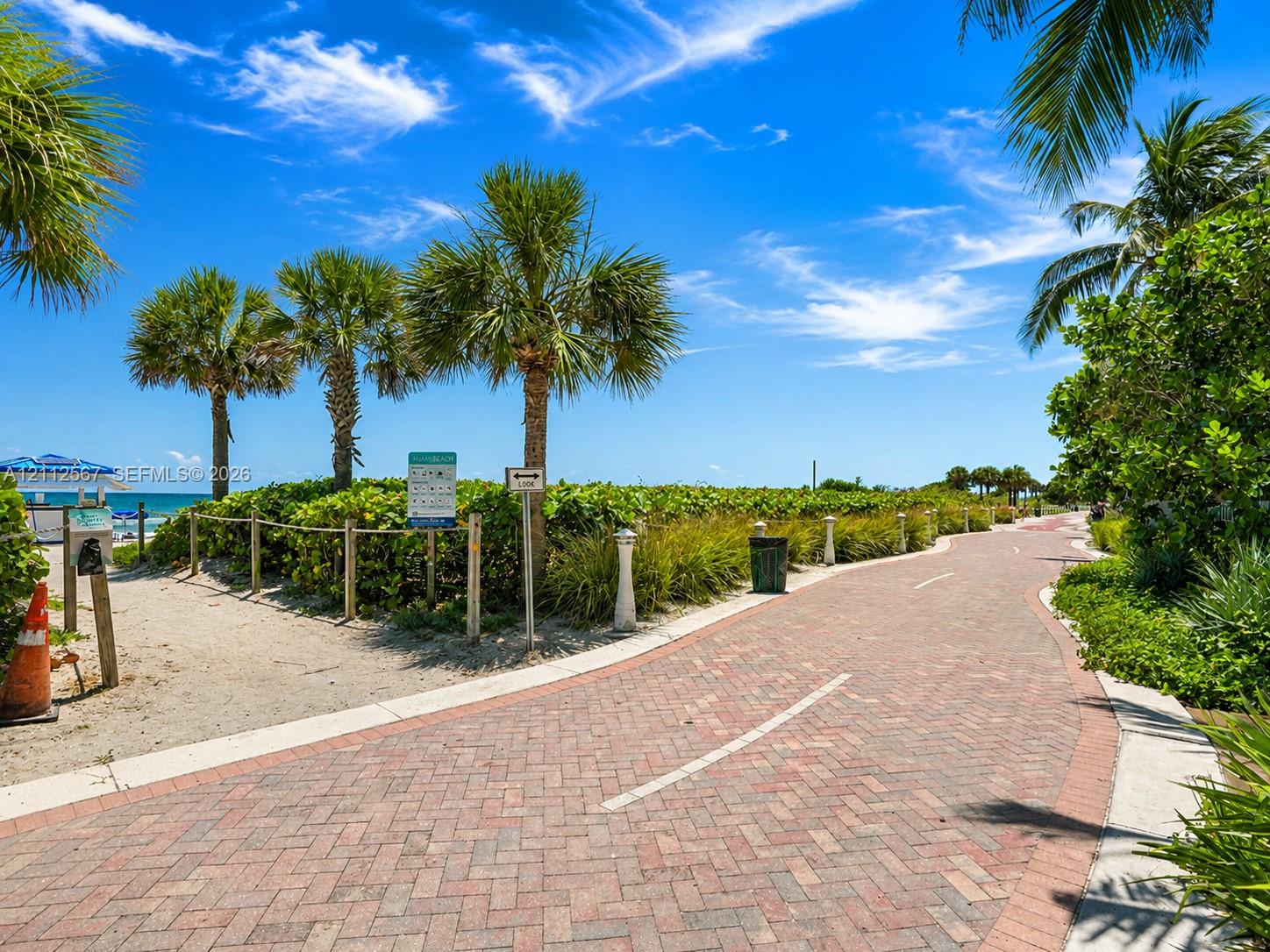 Brick-paver pathway surrounded by palm trees, coastal landscaping, and access to a sandy beach