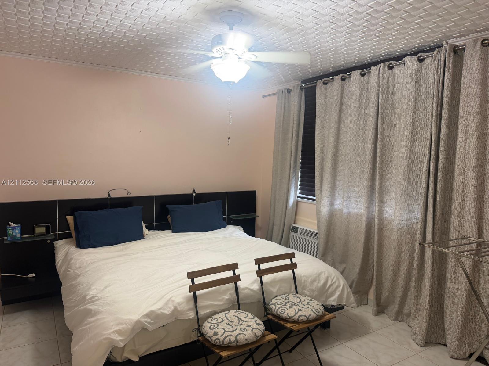 Textured ceiling, tile flooring, built-in black headboard with integrated shelving, and ceiling fan with integrated lighting