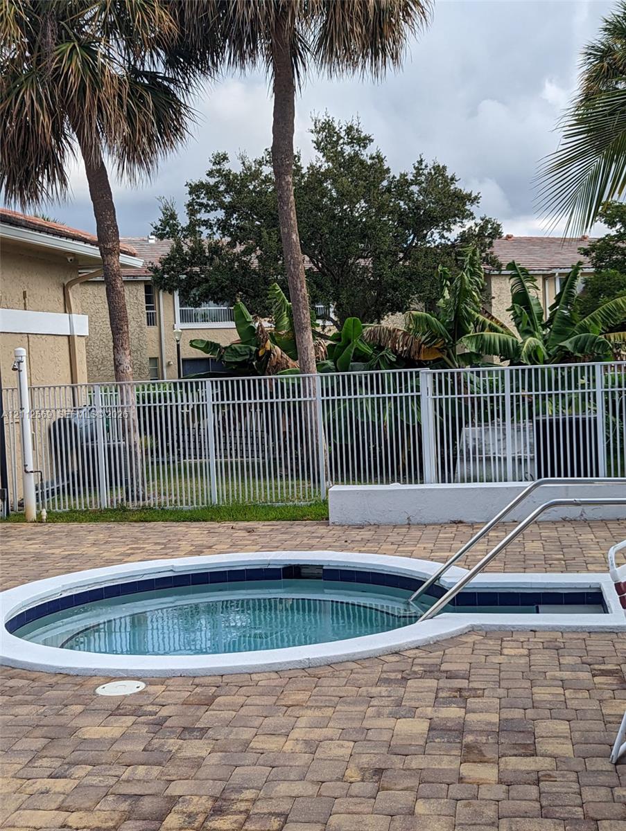 In-ground spa with a tiled surround, paver patio, metal perimeter fencing, and mature palm trees