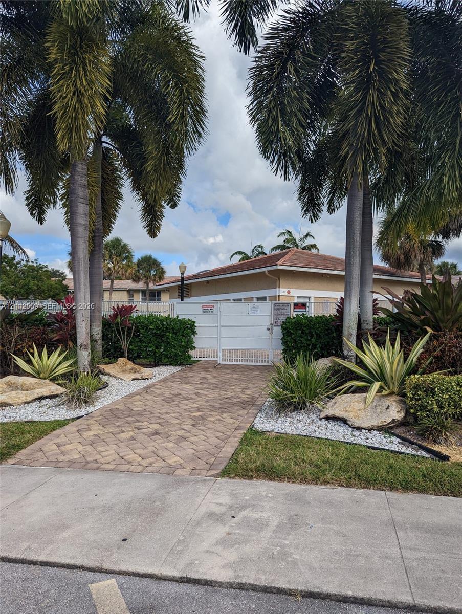 Paver stone walkway leading to a gated entry, accented by mature palm trees, decorative rock borders, and manicured landscaping