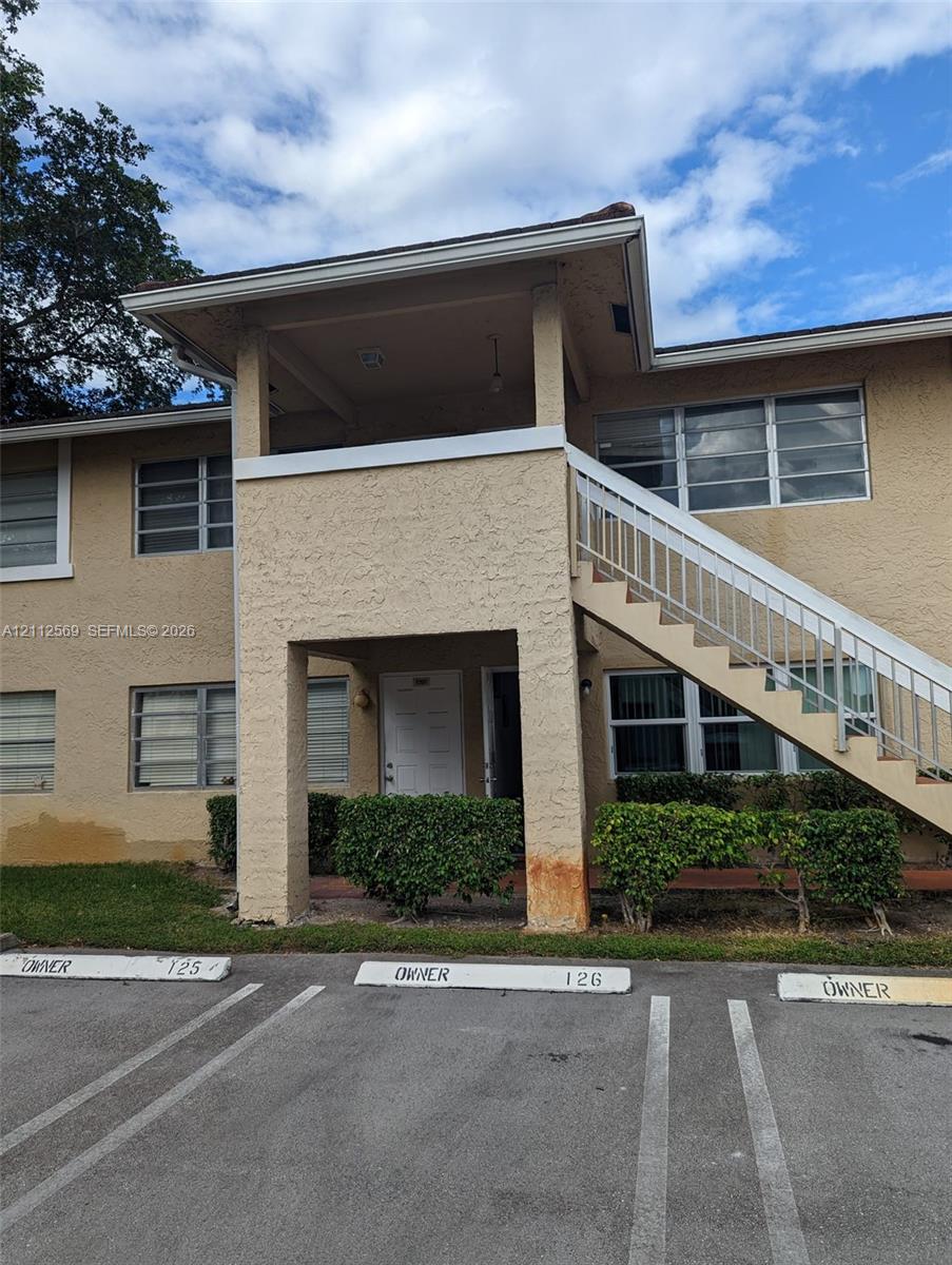 Two-story stucco exterior featuring a covered entryway, external staircase with metal railing, and dedicated parking spaces