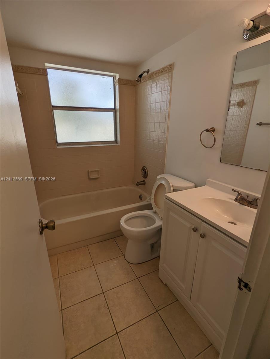 Bathroom featuring tile flooring, a shower-tub combination with tiled surround, a white vanity cabinet, and a single-basin sink