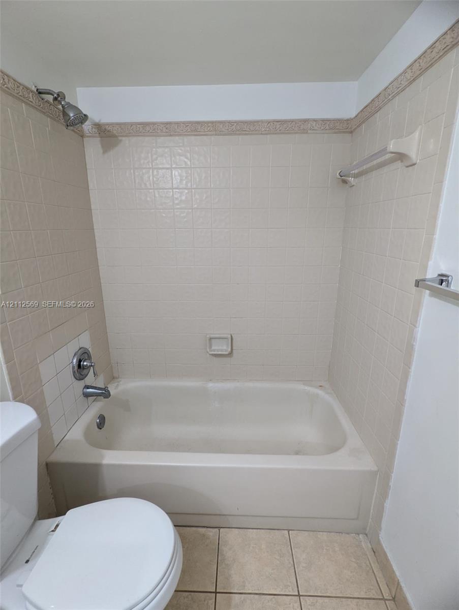 Bathtub and shower combination featuring neutral tile surround, integrated soap dish, chrome fixtures, and a wall-mounted towel bar