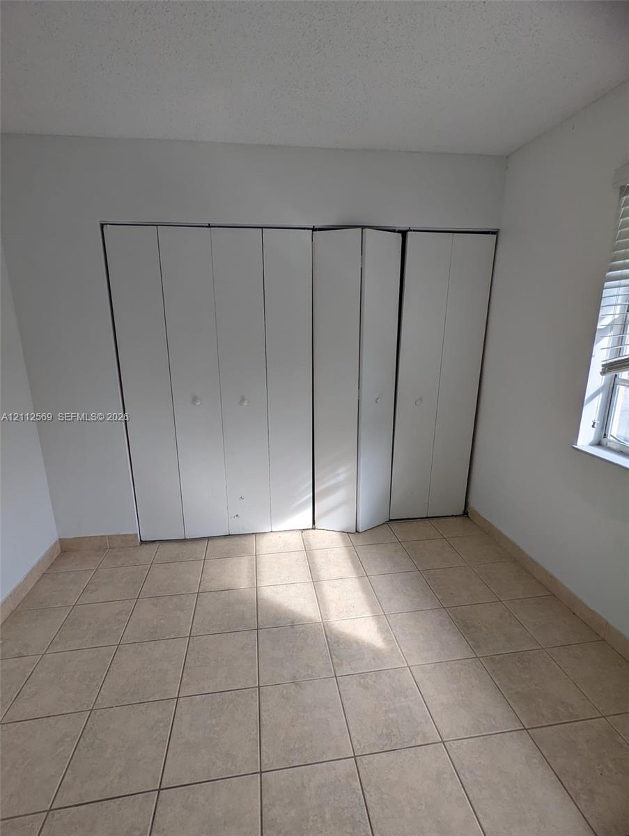 Room featuring neutral ceramic tile flooring, a multi-panel folding closet door, and a single window with horizontal blinds