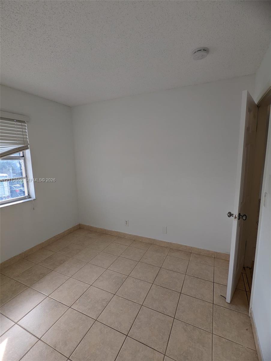 Neutral-toned ceramic tile flooring, single-pane window with horizontal blinds, and a solid-core hinged door