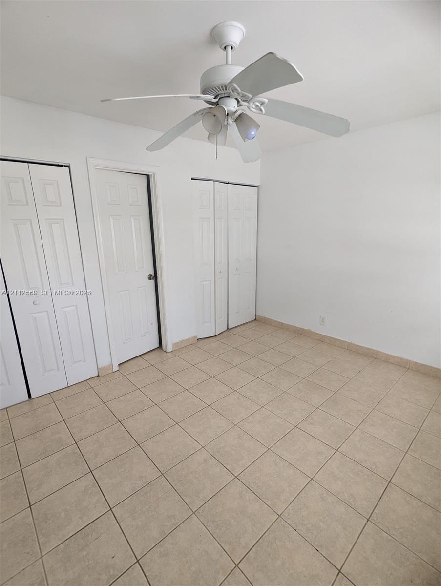 Ceramic tile flooring, white four-panel interior doors, bi-fold closet doors, and a ceiling-mounted light fixture with a fan