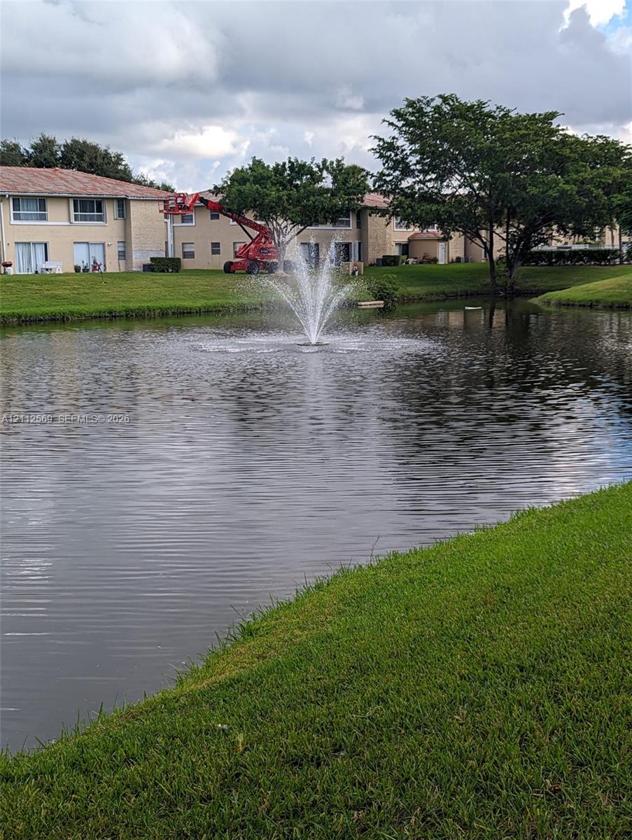 Water feature incorporating a centered fountain set within a natural pond surrounded by manicured turf and mature trees