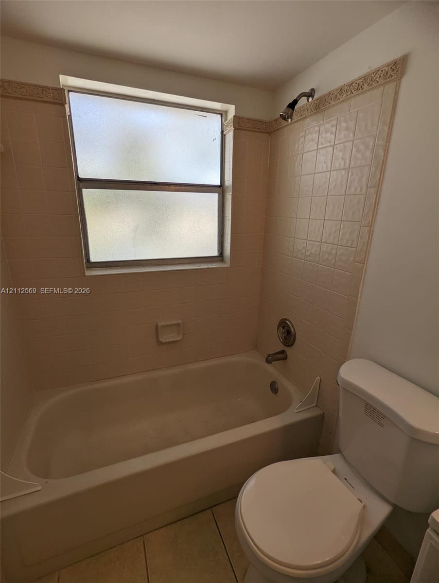 Full bathroom featuring a porcelain-finish soaking tub, ceramic tile surround with decorative trim, a window with frosted glass, and a standard-height toilet