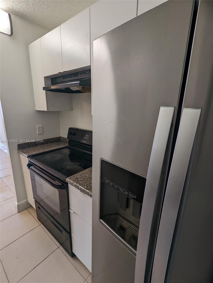 Kitchen featuring flat-panel white cabinetry, speckled stone-finish countertops, black electric range, integrated range hood, and stainless steel side-by-side refrigerator