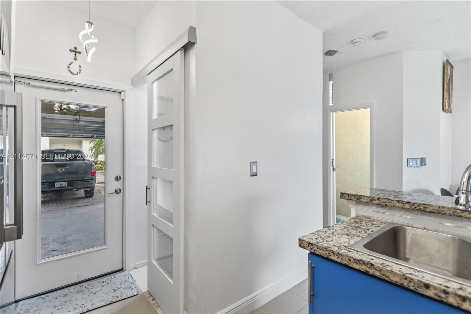 Full-lite glass exterior door, white four-panel sliding barn door with glass inserts, stone-finish countertops, stainless steel undermount sink, and contemporary pendant lighting