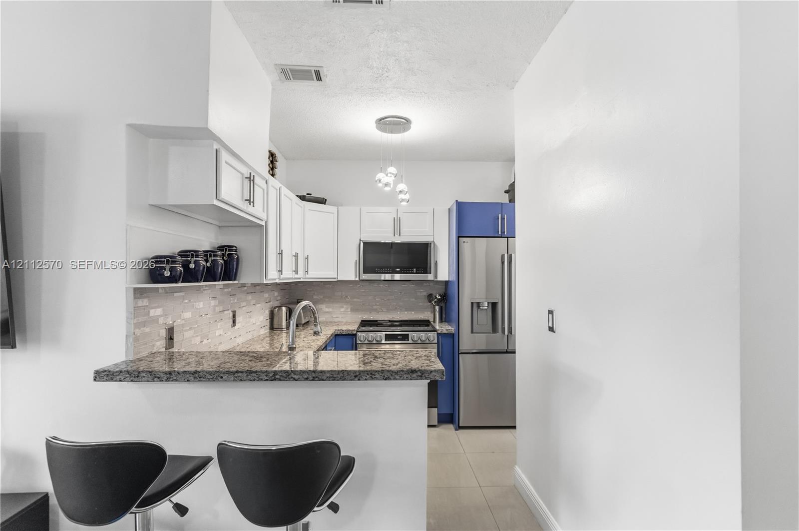 Kitchen featuring stone countertops, a multi-tone cabinetry layout with white upper cabinets, stainless steel appliances, and a tiled backsplash