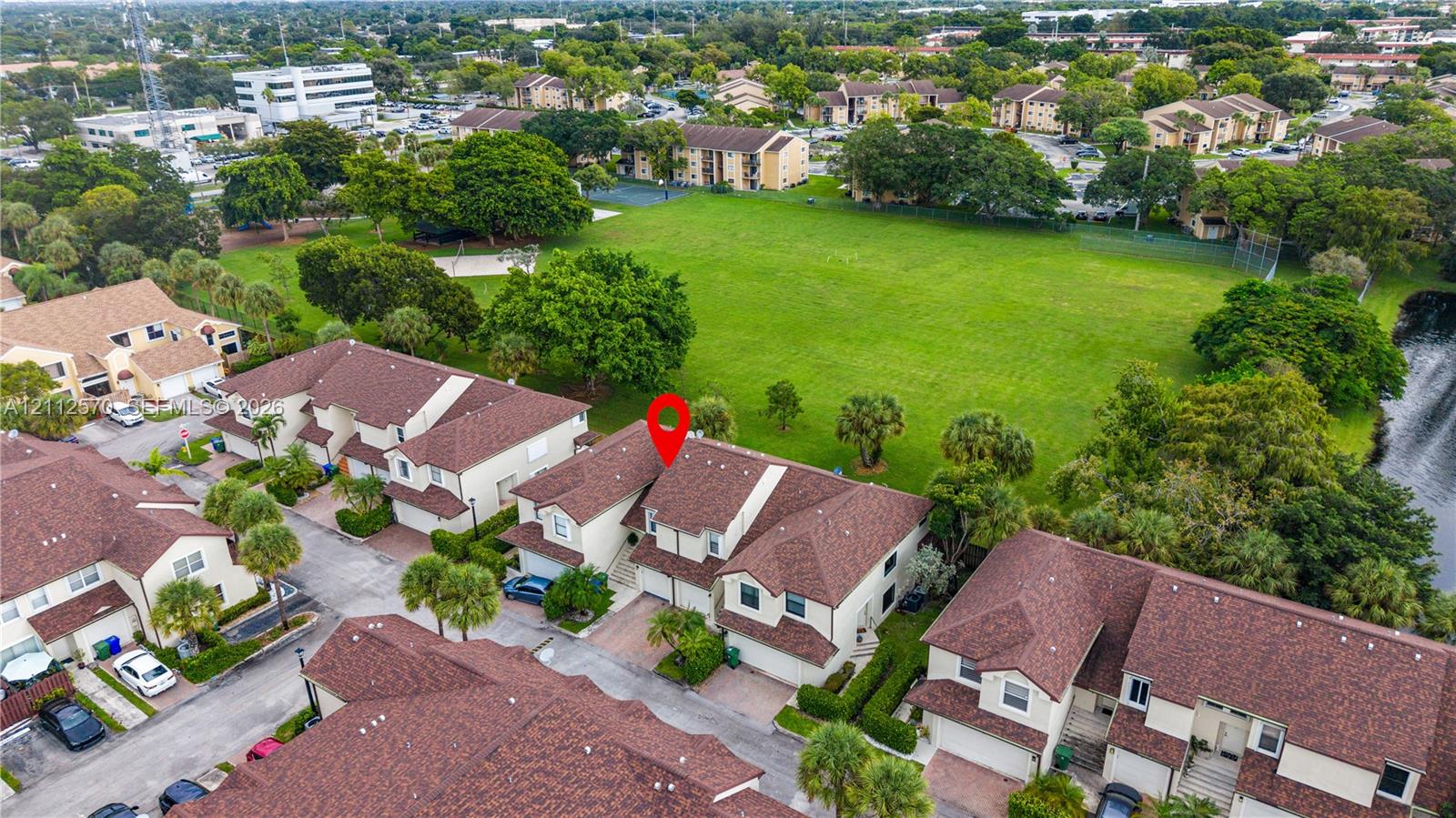 Aerial perspective of multi-family property featuring multi-story architectural design, shingle roofing, brick-paved driveways, and surrounding green space