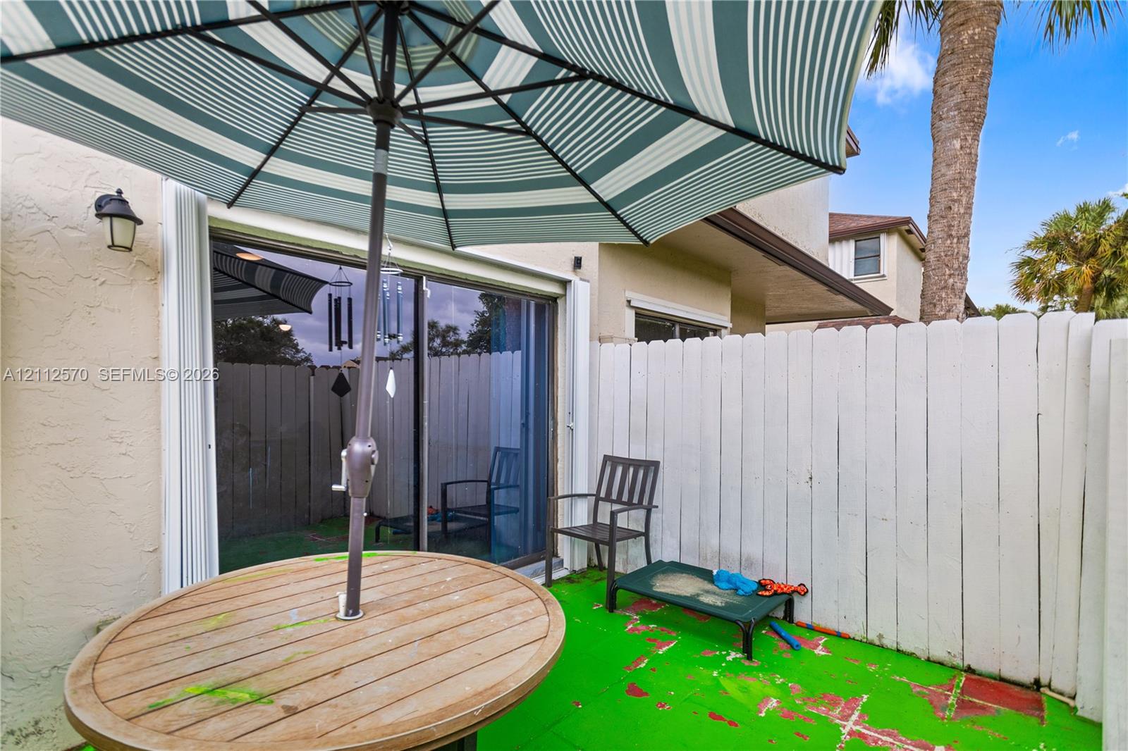 Enclosed patio space featuring a painted concrete surface, tall privacy fencing, and exterior wall-mounted light fixture, providing exterior access via glass sliding doors