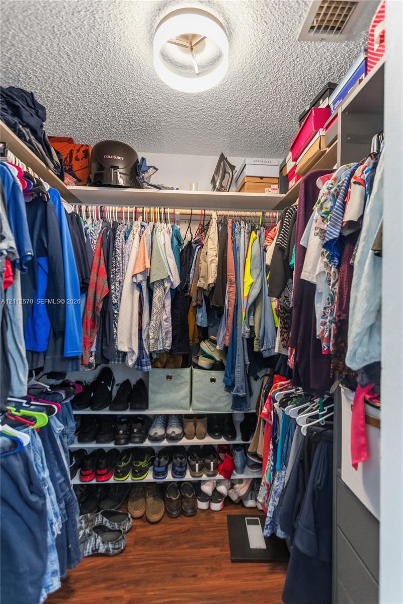 Walk-in closet featuring tiered shelving, built-in hanging rods, and wood-finish flooring