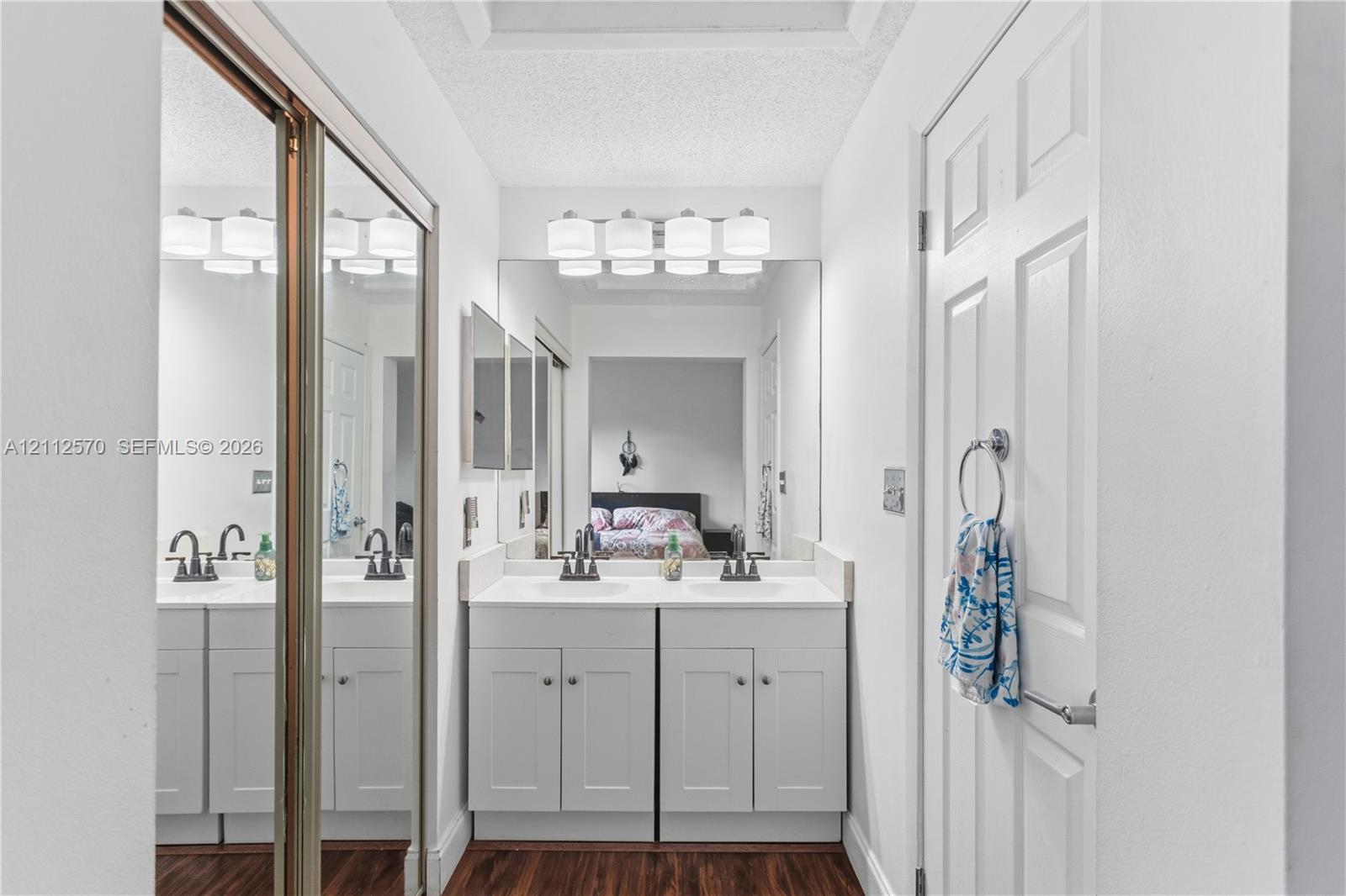 Double vanity featuring white shaker-style cabinetry, solid-surface countertops, dual rectangular drop-in sinks, oil-rubbed bronze fixtures, and a wall-to-wall mirror with overhead light fixture