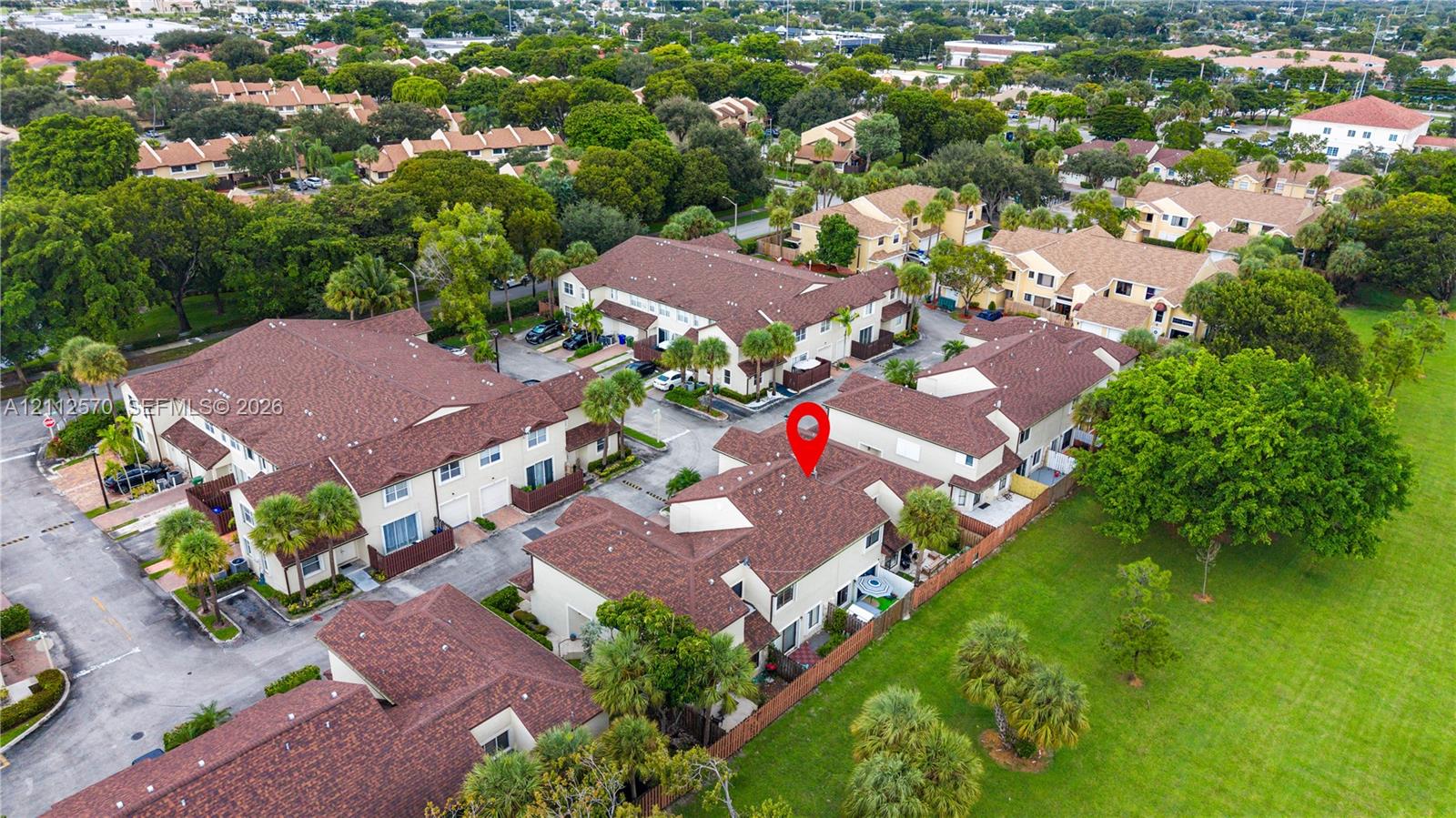 Aerial perspective of a multi-unit property featuring shingle roofing, exterior stucco finishes, palm tree landscaping, and paved parking surfaces