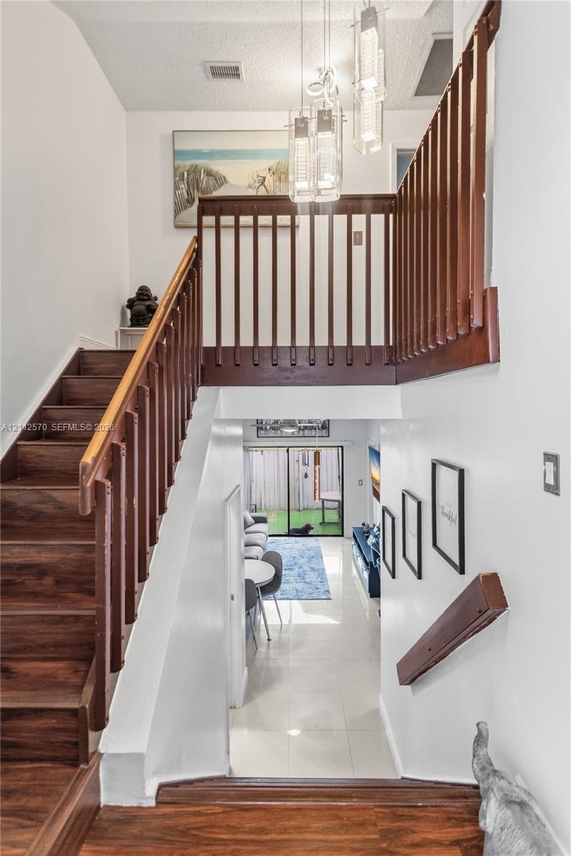 Entryway featuring a wood-finished staircase with matching balustrades, polished tile flooring, and a multi-pendant light fixture Entryway featuring a wood-finished staircase with matching balustrades, polished tile flooring, and a multi-pendant light fixture