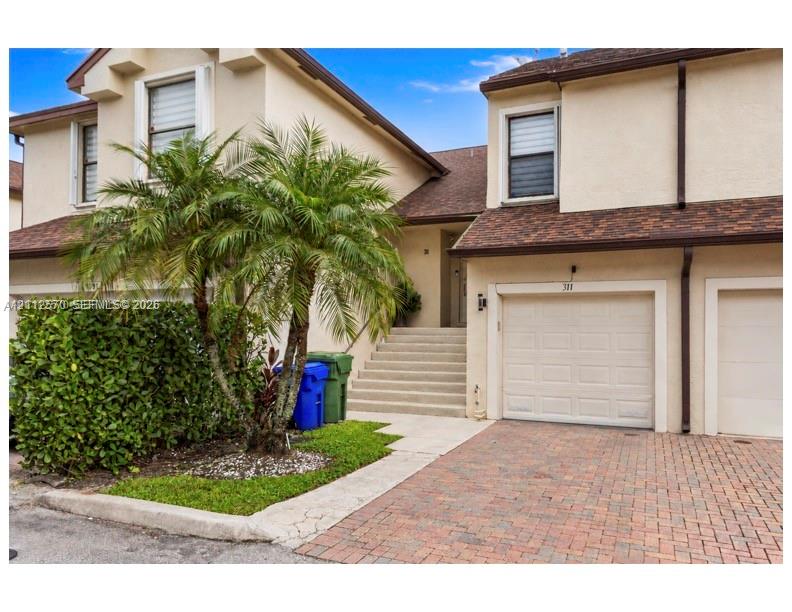 Stucco exterior featuring an attached garage, paver driveway, and concrete stairs leading to the entryway Stucco exterior featuring an attached garage, paver driveway, and concrete stairs leading to the entryway
