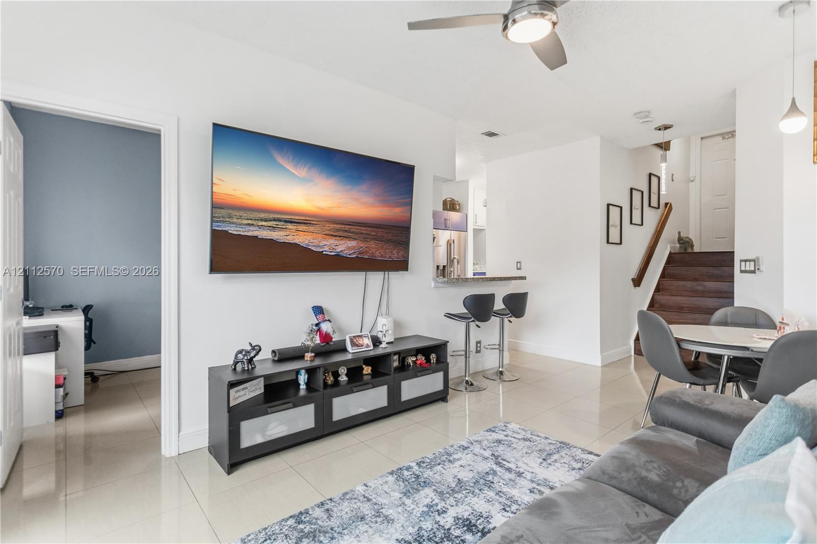 Large format tile flooring, ceiling fan with integrated lighting, kitchen breakfast bar, and wooden staircase with handrail