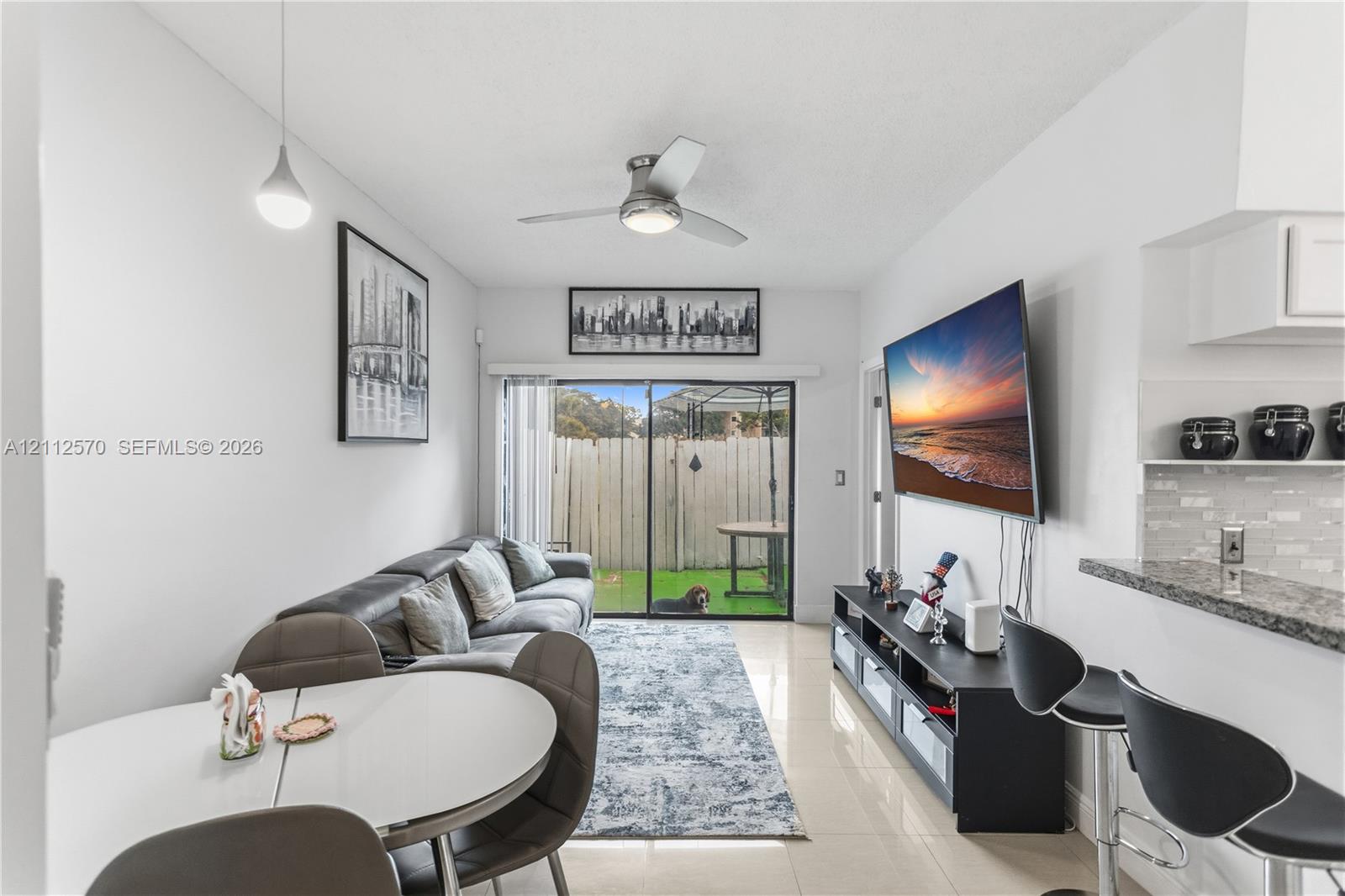 Neutral-toned tile flooring, ceiling-mounted fan with integrated light, sliding glass doors, and a stone-surface breakfast bar Neutral-toned tile flooring, ceiling-mounted fan with integrated light, sliding glass doors, and a stone-surface breakfast bar