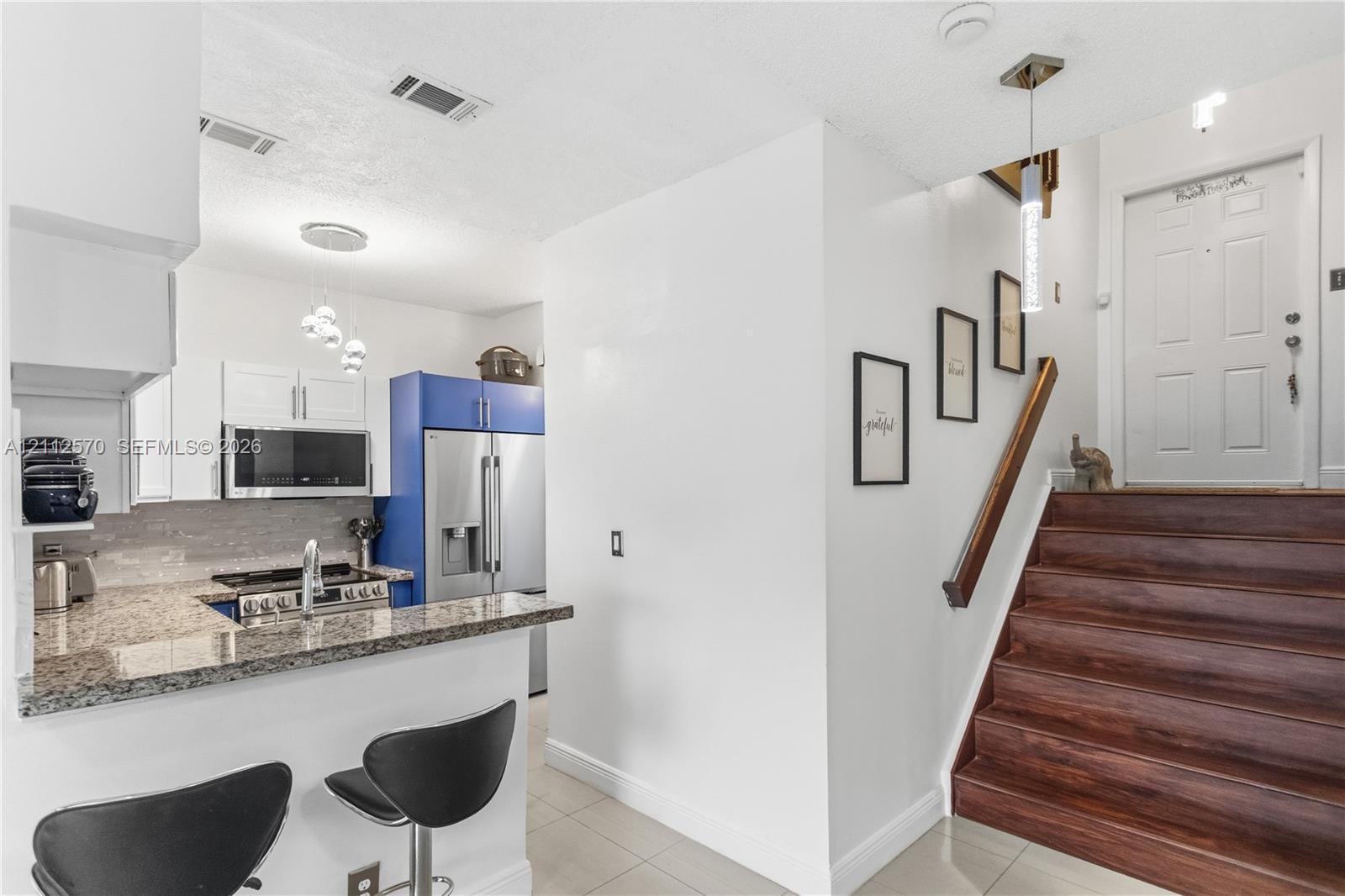 Kitchen featuring stone countertops, stainless steel appliances, and white cabinetry, complemented by a staircase with wood-finish treads and a metal handrail