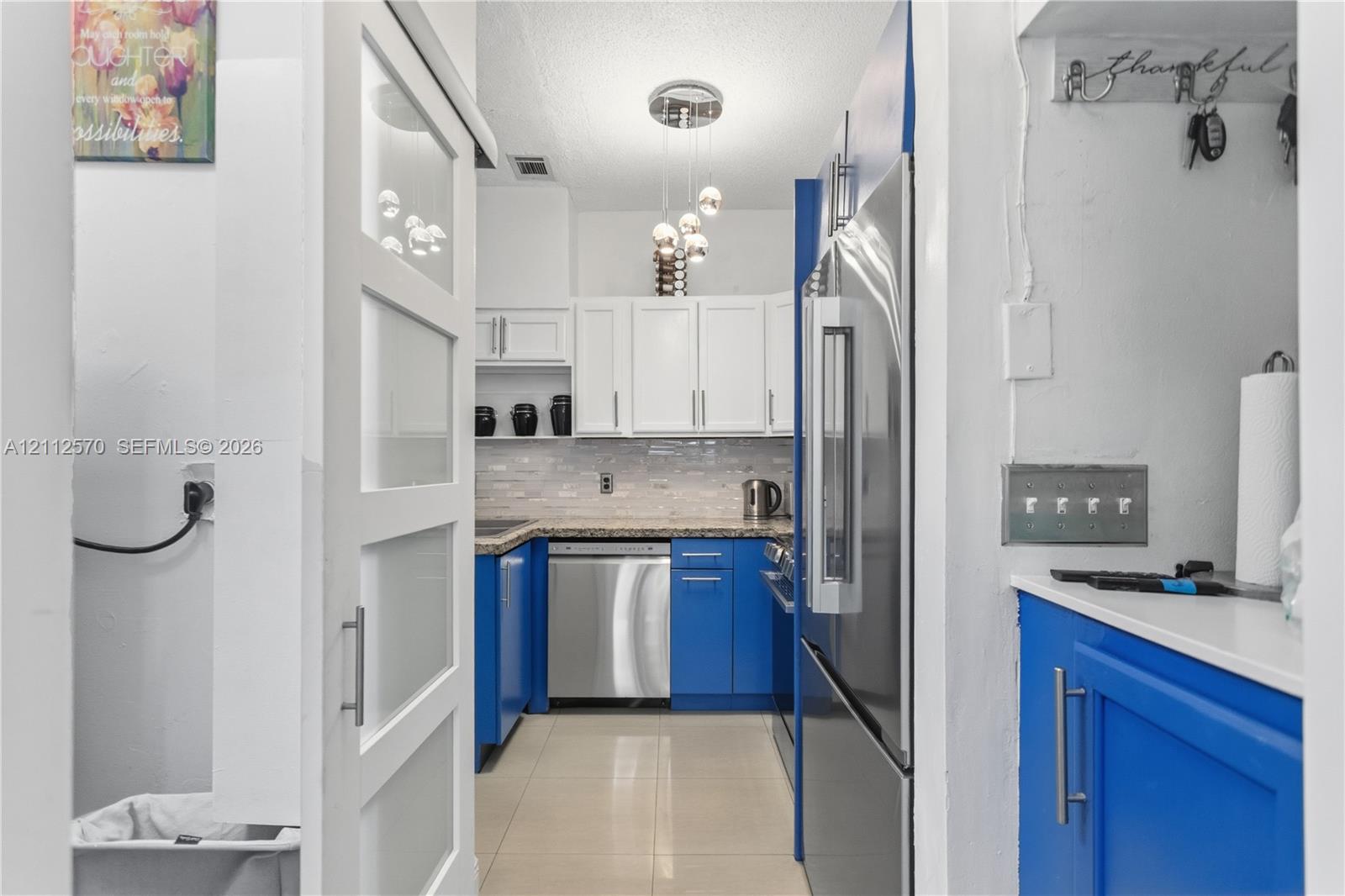 Kitchen featuring blue lower cabinetry, white upper cabinetry, tiled backsplash, stainless steel appliances, and a multi-pendant light fixture