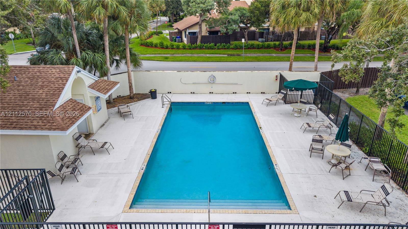 Rectangular swimming pool featuring integrated steps, surrounded by a paved deck, perimeter fencing, and an attached cabana structure