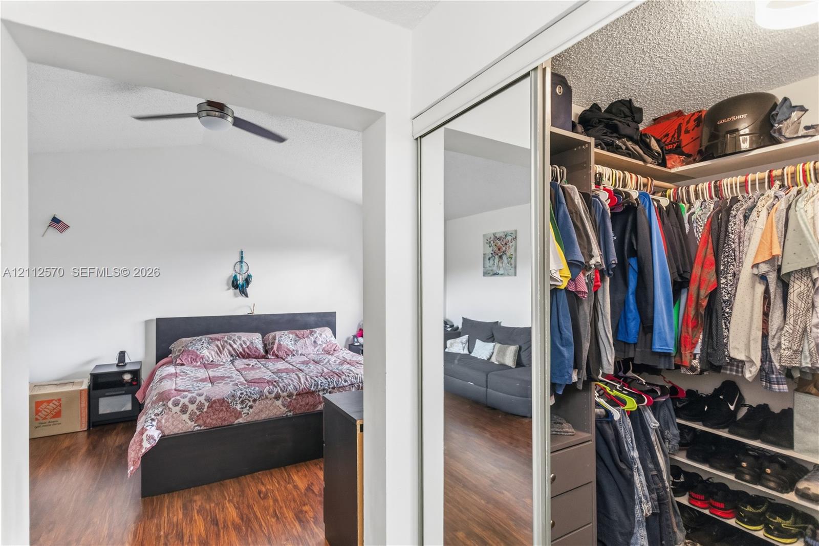 Wood-finish flooring, vaulted ceilings, ceiling fan, and walk-in closet featuring mirrored sliding doors and built-in shelving