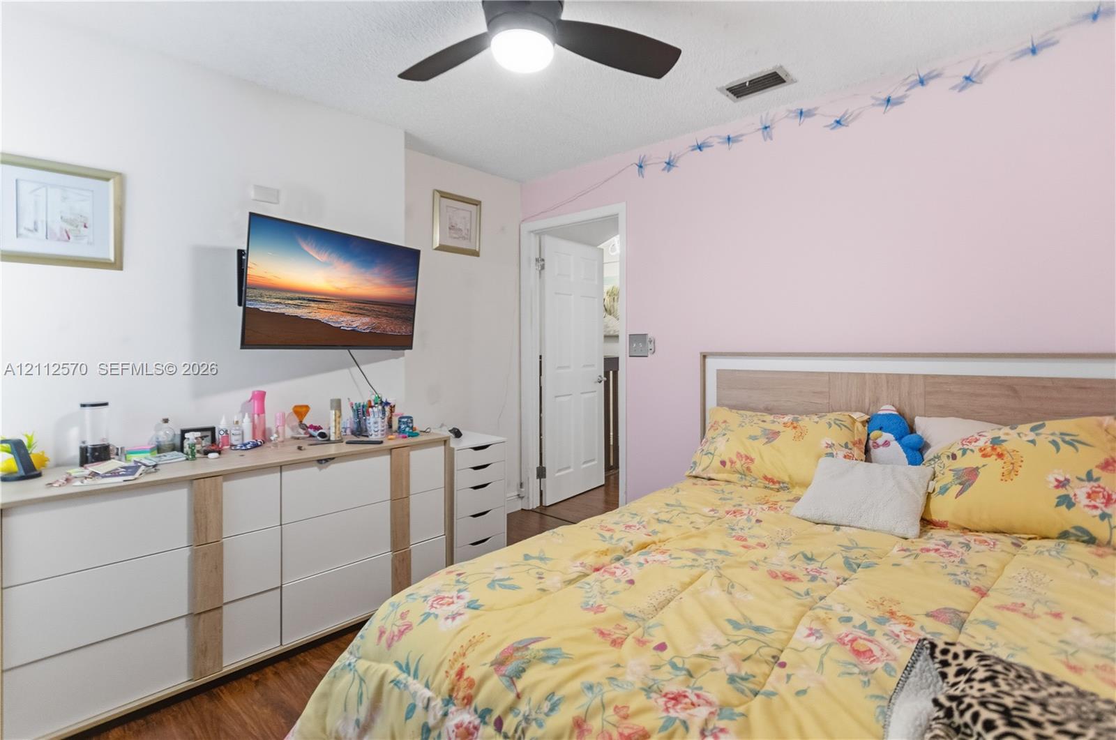 Bedroom featuring wood-finish flooring, a ceiling fan with integrated lighting, and a six-panel door