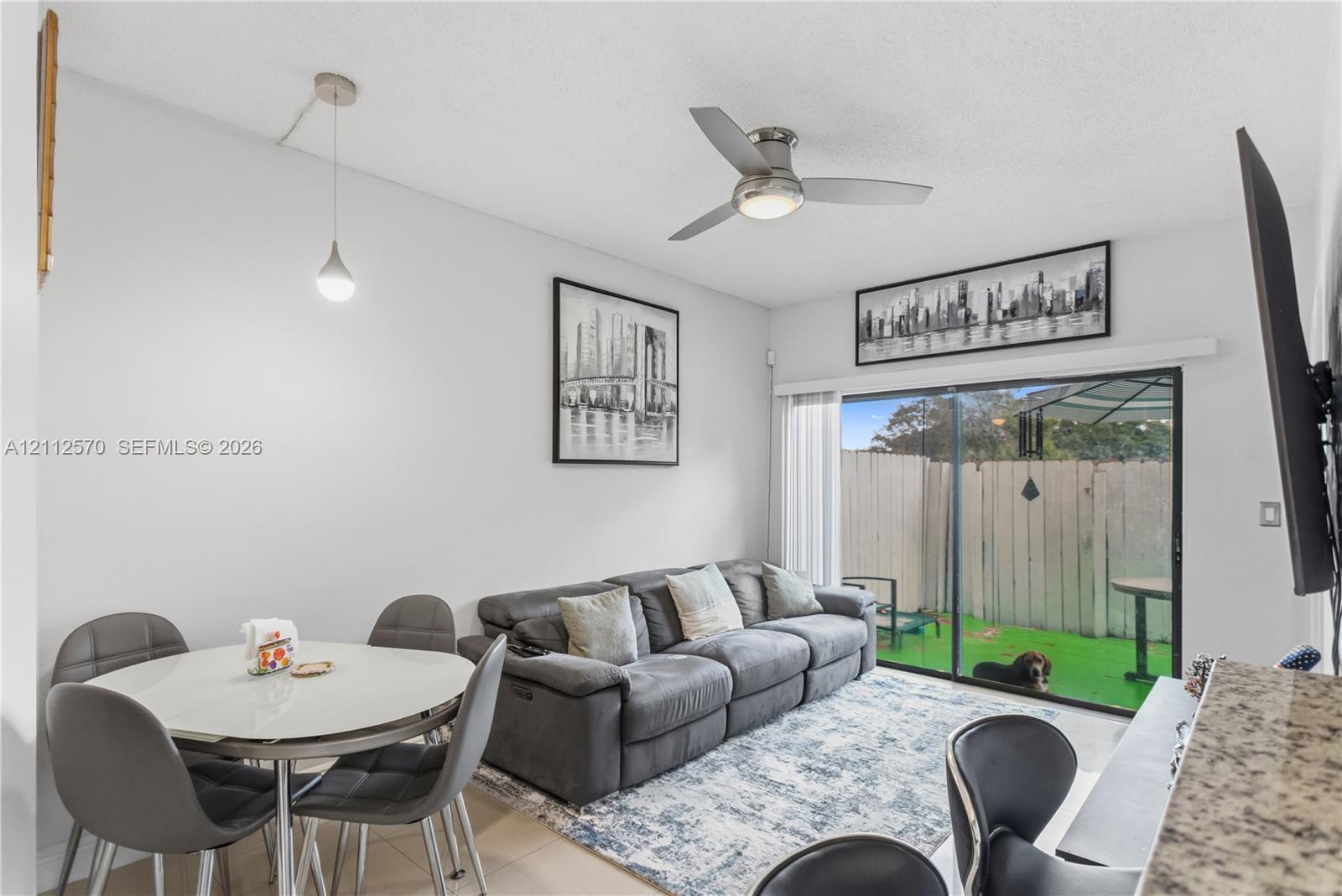 Living space featuring a ceiling fan, a pendant light fixture, and a sliding glass door providing external access to a fenced patio area Living space featuring a ceiling fan, a pendant light fixture, and a sliding glass door providing external access to a fenced patio area