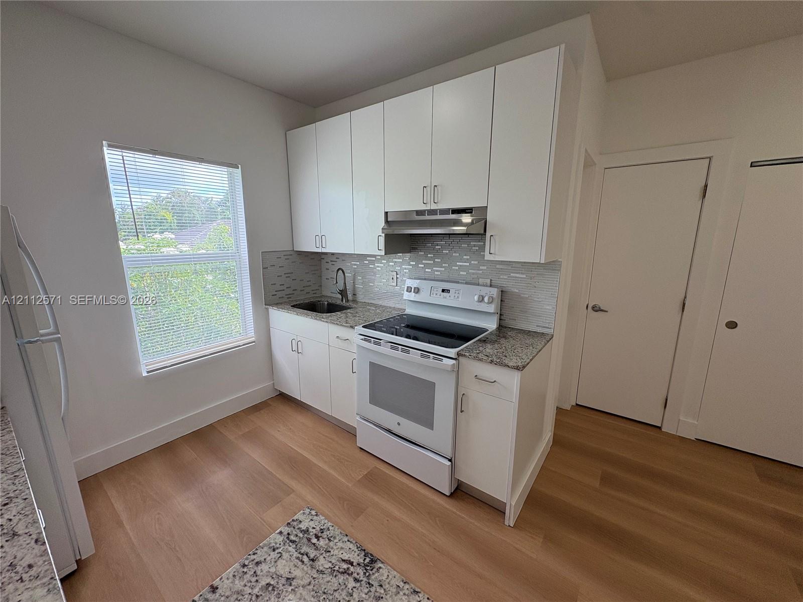 Kitchen featuring white cabinetry, stone-finish countertops, tile backsplash, wood-finish flooring, and white range