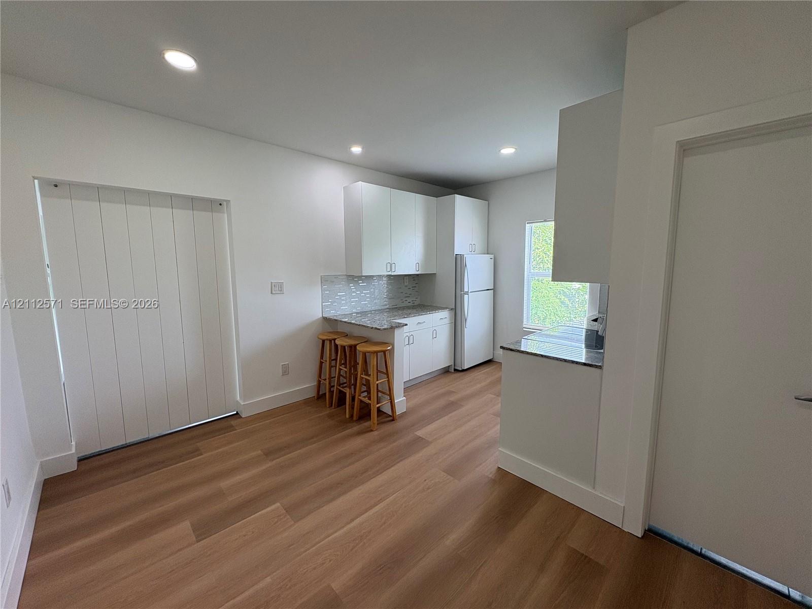 Kitchen featuring white cabinetry, stone-finish countertops, tile backsplash, and wood-finish flooring